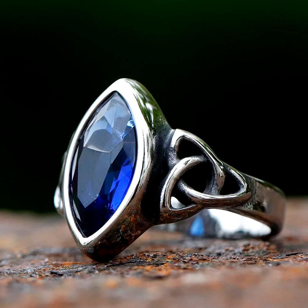 A stainless steel ring with a Celtic knot design and a red gemstone in the center.