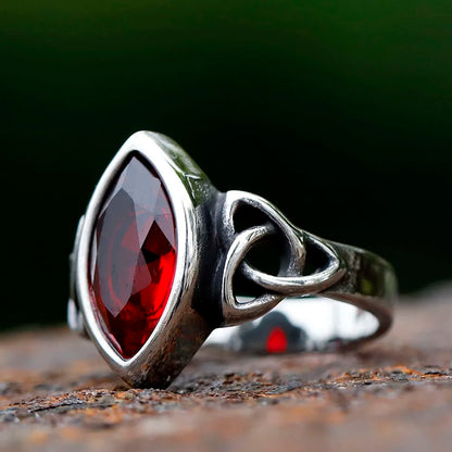 A stainless steel ring with a Celtic knot design and a red gemstone in the center.