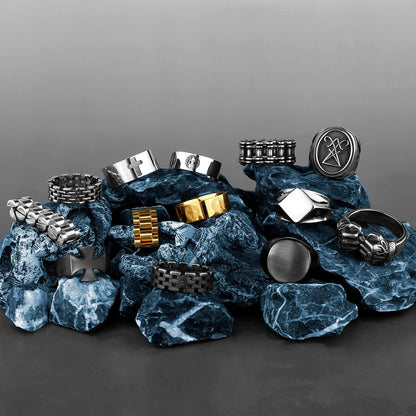 Assortment of Viking stainless steel rings in gold, silver, and black finishes displayed on blue rocks.